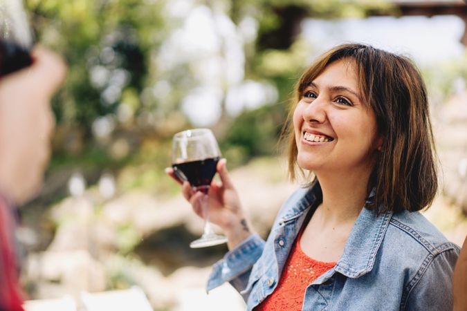 Portrait of an happy young woman talking with friends holding a glass of red wine