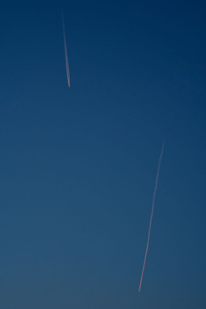 Two airplane contrails crossing blue evening sky