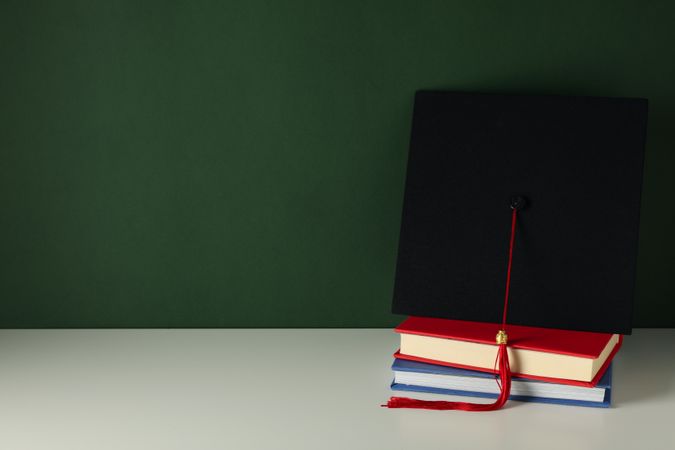 Graduation hat with books on a table on a dark background.