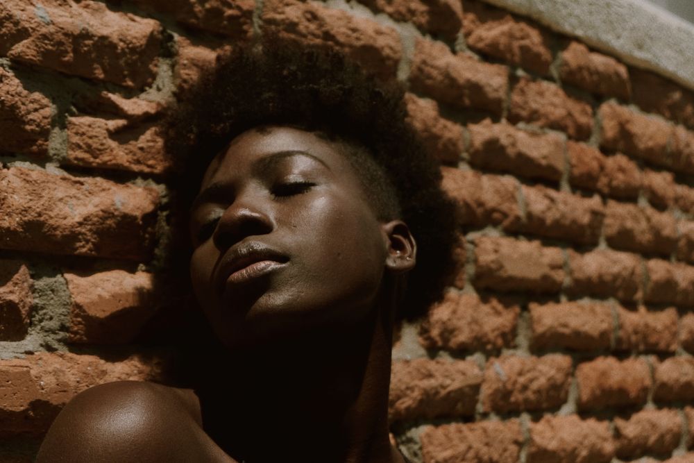 Young Black woman with eyes closed against wall