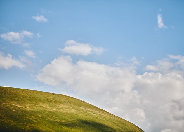 Top of a grassy hill under a blue sky with clouds