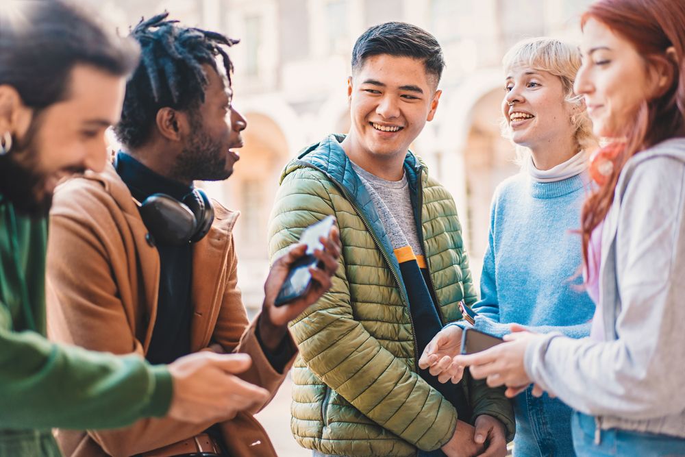 Group of diverse university students smiling and engaging with smartphones during a break in the campus courtyard
