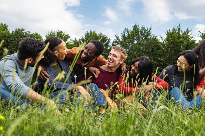 Multiracial community of happy friends having fun sitting in the grass