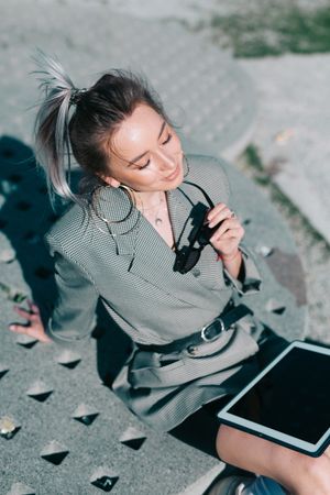 Woman sitting on asphalt with tablet and enjoying sun
