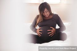Pregnant woman touching her belly with hands while sitting on bed at home 4ZdaO0