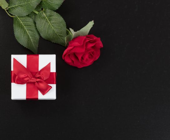Gift and a single red rose on dark stone