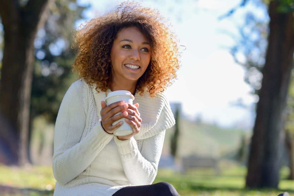 Happy woman looking in the distance while holding warm drink sitting in park