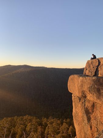 Sideview of single man sitting on cliff overlooking forest