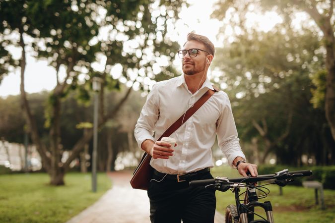 Businessman listening to music and enjoying coffee while walking to office with his bike