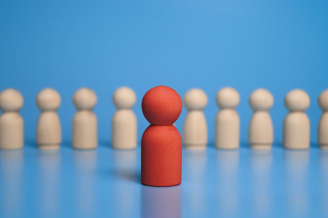 red wooden figure stand to the wooden group crowd. isolated on blue background. leadership and teamwork concept