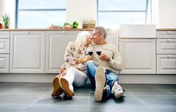 Cute older couple about to kiss on the kitchen floor with red wine