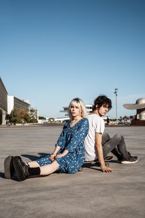 Trendy couple sitting together on skateboard on street