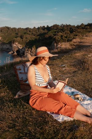 Woman reading on mat for picnic on seashore