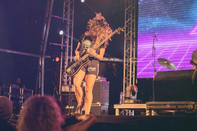 Woman with curly hair playing electric guitar on stage at night