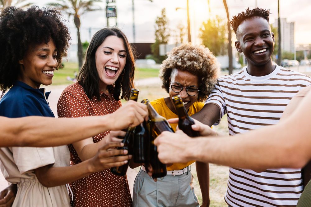 Happy young multiracial friends celebrating and cheering with beer at summer party outdoors