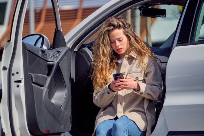 Focused woman browsing smartphone in car with opened door