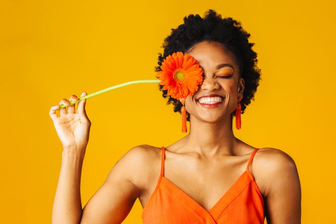 Happy Black woman holding a flower over her eye