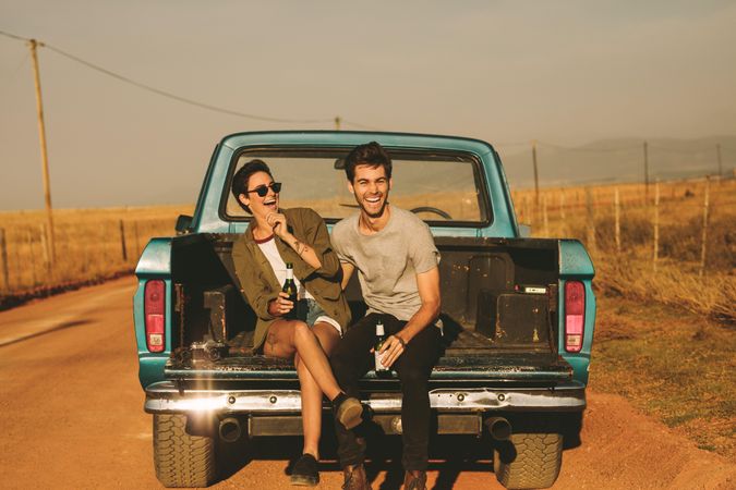 Joyful man and woman holding bottled drinks enjoying country road trip