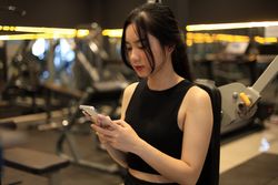Young Female Sitting on Workout Bench in the Gym While Holding Mobile Phone