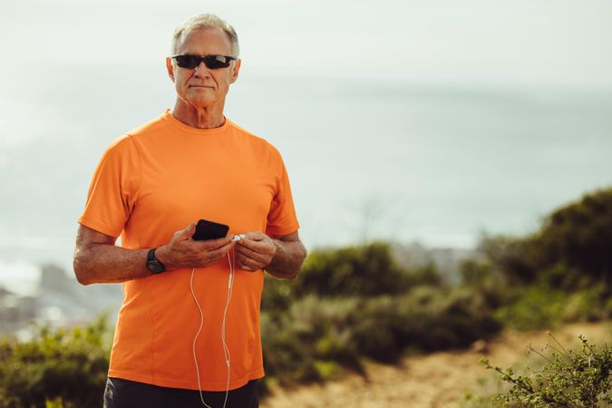 Mature man in fitness wear standing outdoors holding a mobile phone