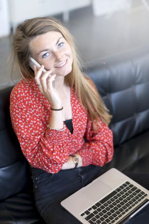 Above view of a woman using an smartphone while talking and sitting on a sofa in the living room at home