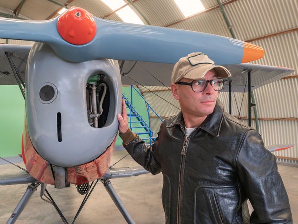 Confident pilot beside retro plane in hangar