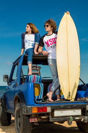 Guy with surfboard and woman on roof of car