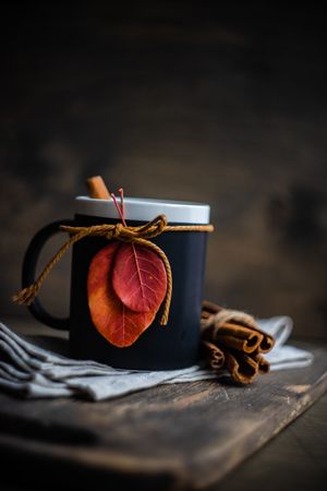 Mug with cinnamon sticks decorated with autumn leaves on table