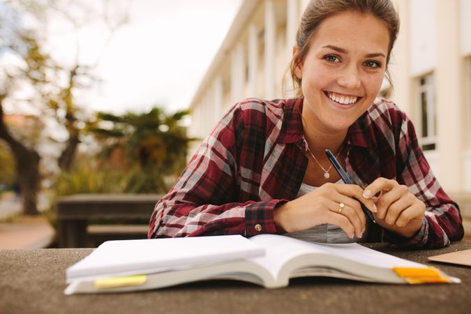 Smiling female student sitting at college campus with books