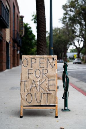 Sign on city sidewalk posted by restaurant indicating take out food available