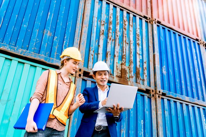 Two colleagues checking plans on laptop on dock with containers