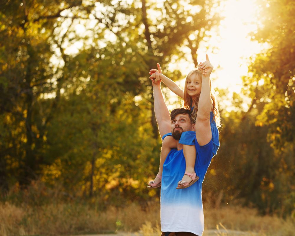 Dad with daughter on shoulders dressed in blue walking along forest path