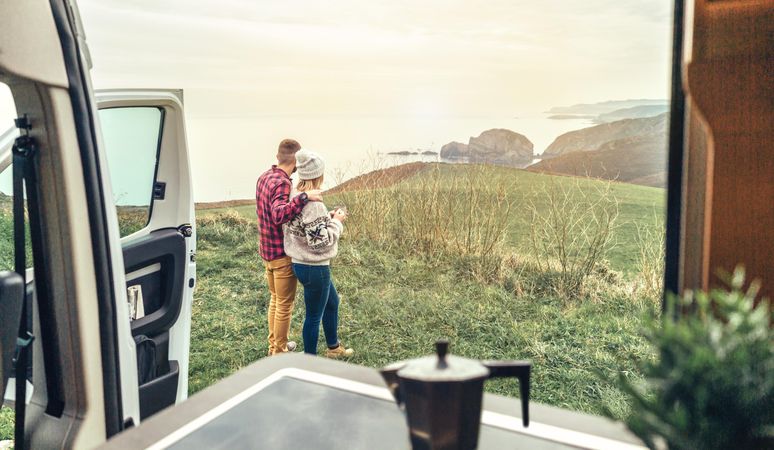 Couple enjoying beautiful morning view outside of camper van with cup of coffee