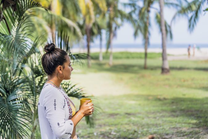 Relaxed woman enjoying hot drink and standing on exotic lawn