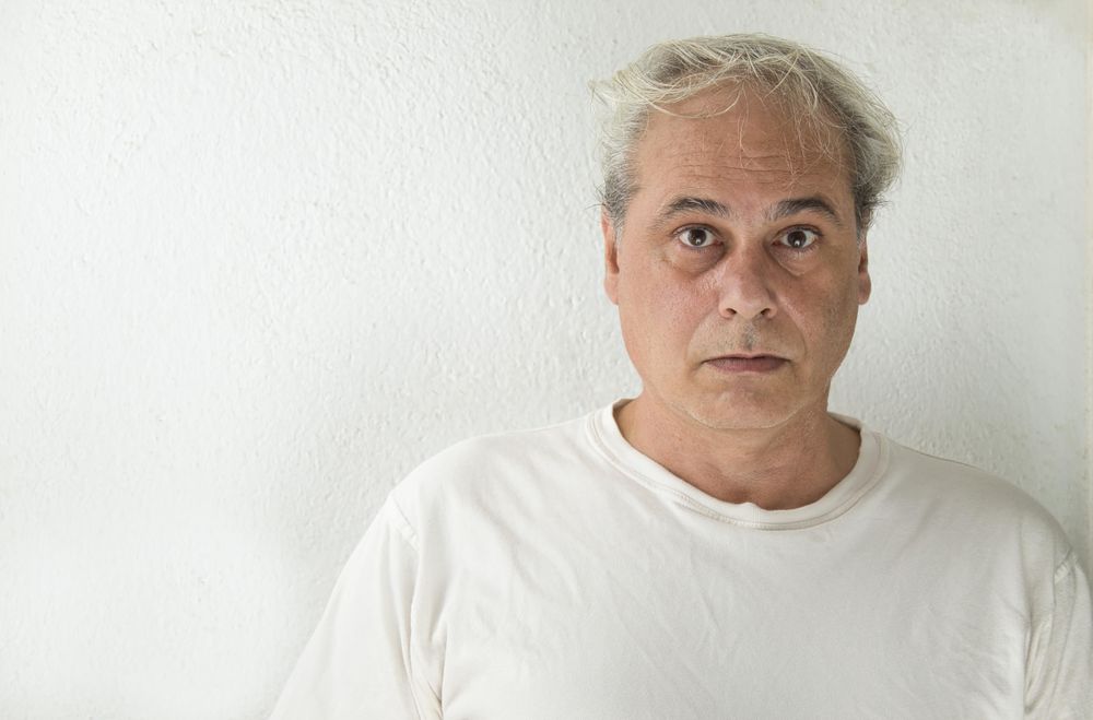 Portrait of surprised middle aged man in light shirt against light wall