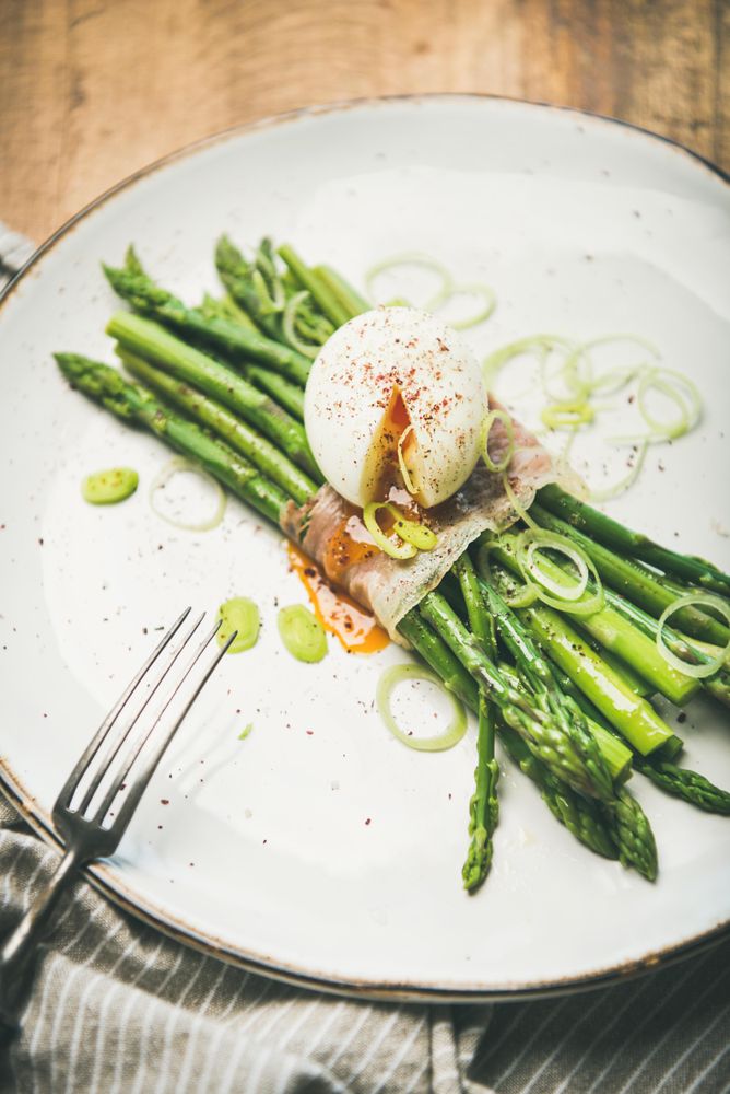 Asparagus and soft boiled egg on plate with fork, on wooden table