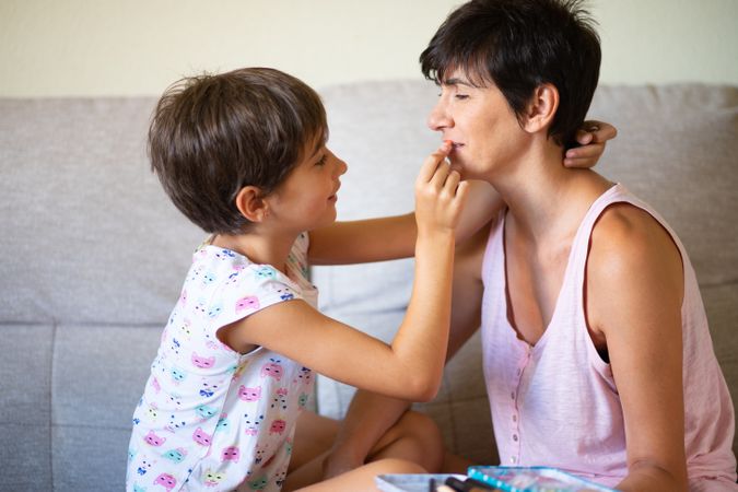 Little girl putting lipstick on her mother
