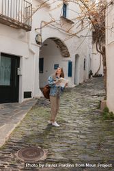 Woman standing in middle of narrow town street holding map and looking up 0v3eR5