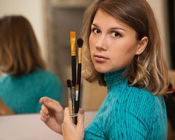 Female artist in green shirt holding paintbrushes