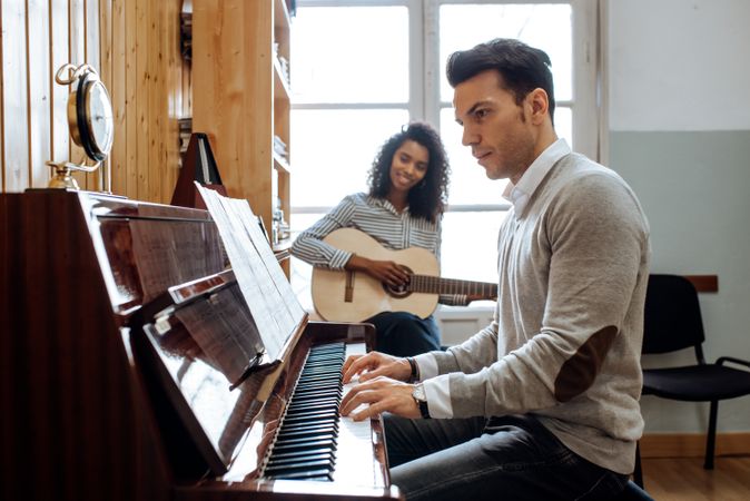 Man playing piano near woman playing guitar in studio
