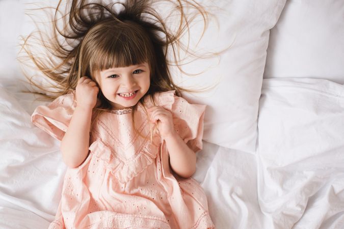 Smiling girl in pink dress lying on bed