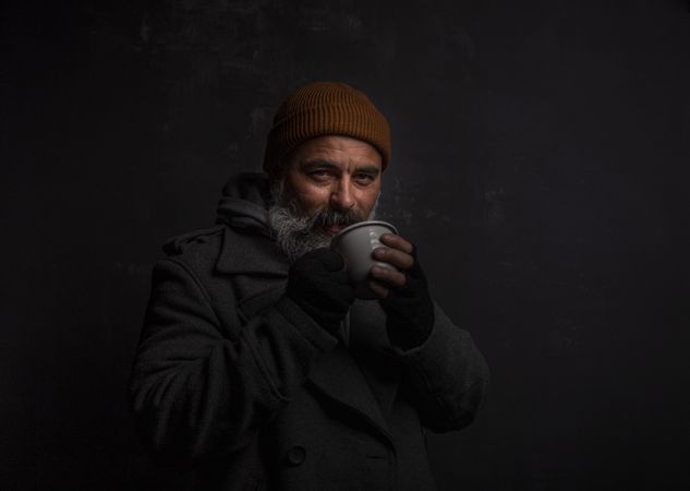 Homeless smiling middle-aged man with a gray beard holding a cup of hot tea