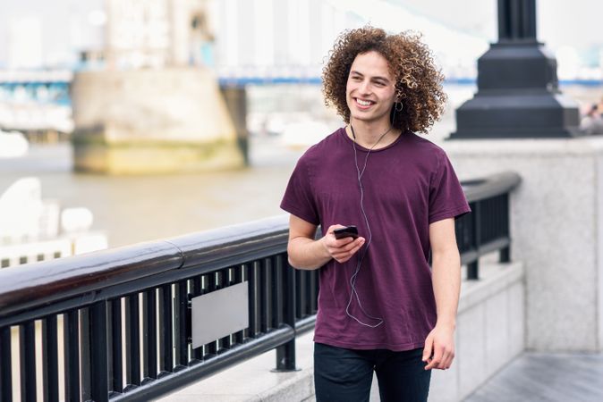 Curly haired man smiling while listening to music along river walk