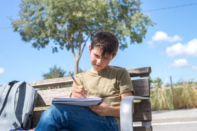 Teenager sitting on bench drawing in notebook