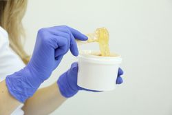 Young woman holding liquid yellow paste for sugaring on plain background, copy space