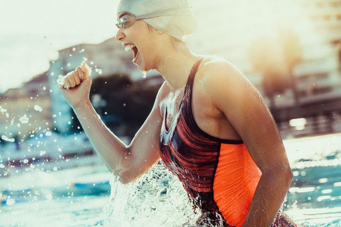 Woman swimmer cheering success in pool wearing swim goggles and cap