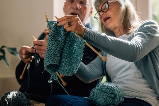 Woman teaching her husband the art of knitting wool clothes.