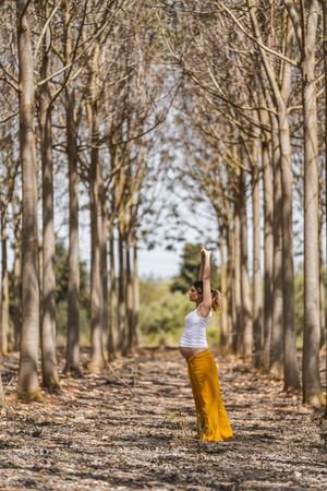 Adult expectant mother practicing yoga in park during sunny day