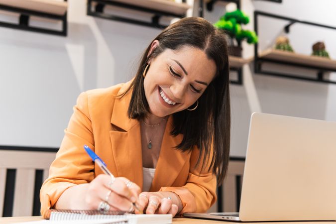 Smiling woman taking notes in notebook during work in cafe