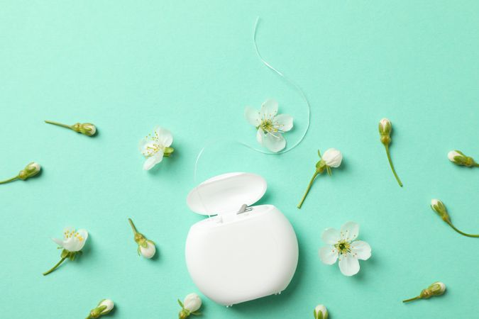 Dental floss and flowers on mint background, top view